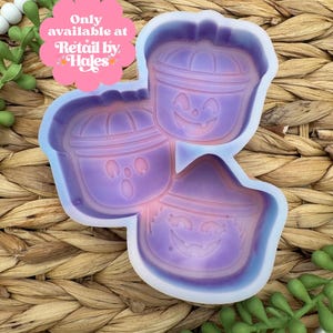 May include: A purple silicone mold featuring three Halloween-themed designs: two jack-o'-lanterns and a witch's hat with a smiling face. The text "Only available at Retail by Hales" is visible. The mold is on a woven background.