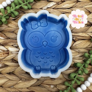 May include: A blue silicone mold in the shape of an owl with a bow on its head. The owl has large eyes and a series of curved lines on its chest. The text "Retail by Hales" is in a pink and white floral design.