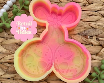 May include: A two-part silicone mold in shades of pink, yellow, and orange, shaped like cherries. Each cherry half features a detailed mask design. The mold is on a woven wicker background, with the text "Retail by Hales" on a pink flower-shaped sticker.