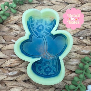 May include: A light green and blue silicone mold in the shape of a heart with a leopard print design. The mold has three heart shapes connected together. The text "Retail by Hales" is in a pink flower-shaped graphic.