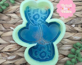 May include: A light green and blue silicone mold in the shape of a heart with a leopard print design. The mold has three heart shapes connected together. The text "Retail by Hales" is in a pink flower-shaped graphic.
