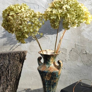 May include: Dried hydrangea flowers in a blue and brown ceramic vase with a rustic wooden background.