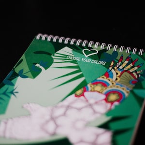 May include: A green spiral bound notebook with a colorful illustration of hands and the text "CHOOSE YOUR COLORS" with a heart symbol.