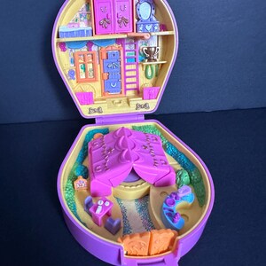 Puede incluir: Un juego de Polly Pocket vintage morado y amarillo, abierto para revelar una casa en miniatura con muebles y una tienda de campa&ntilde;a. El juego presenta una peque&ntilde;a escalera, un armario y una mesa con sillas.