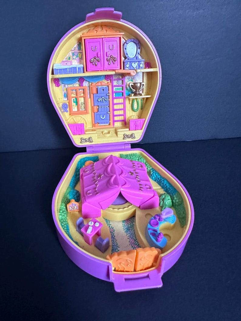 Puede incluir: Un juego de Polly Pocket vintage morado y amarillo, abierto para revelar una casa en miniatura con muebles y una tienda de campa&ntilde;a. El juego presenta una peque&ntilde;a escalera, un armario y una mesa con sillas.