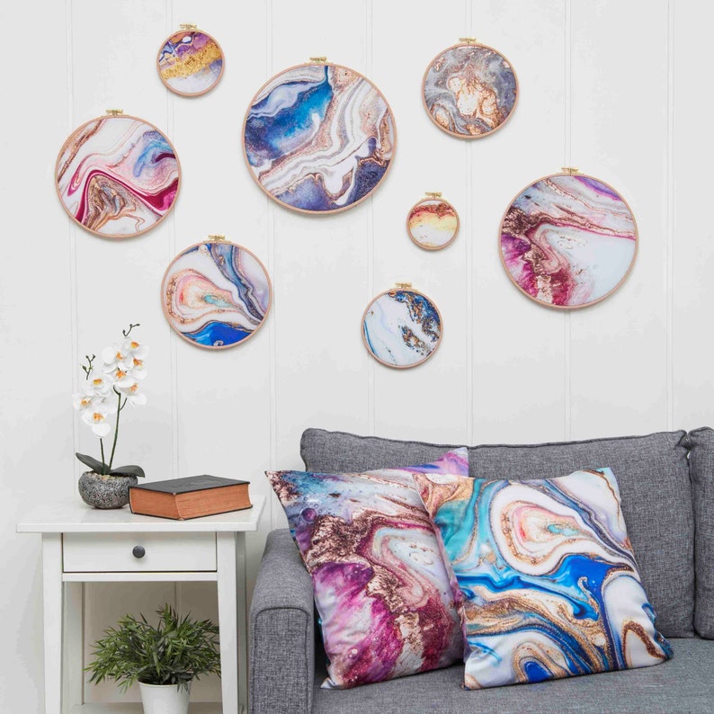 May include: A living room featuring a grey sofa with two cushions displaying abstract marble patterns in shades of blue, pink, and gold. The wall behind the sofa is adorned with eight circular wall hangings showcasing similar abstract marble designs in a variety of colours.