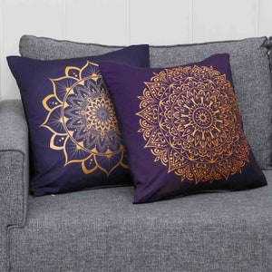 Puede incluir: Dos almohadas decorativas con fondo morado oscuro y dise&ntilde;os de mandalas dorados.