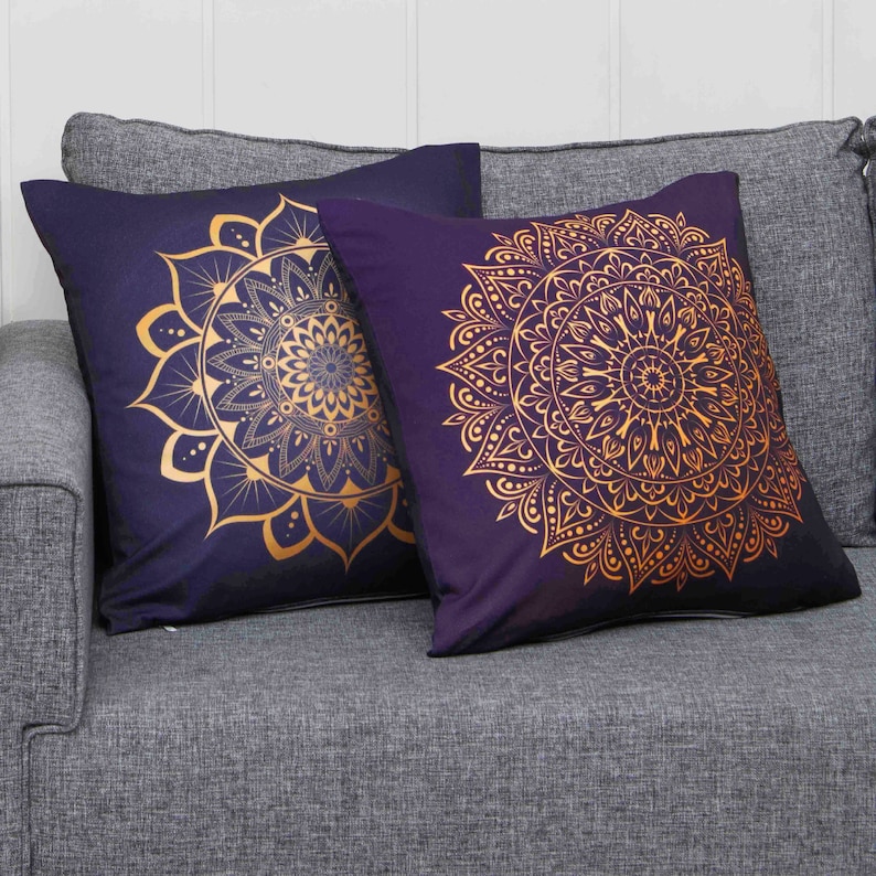 Puede incluir: Dos almohadas decorativas con fondo morado oscuro y dise&ntilde;os de mandalas dorados.