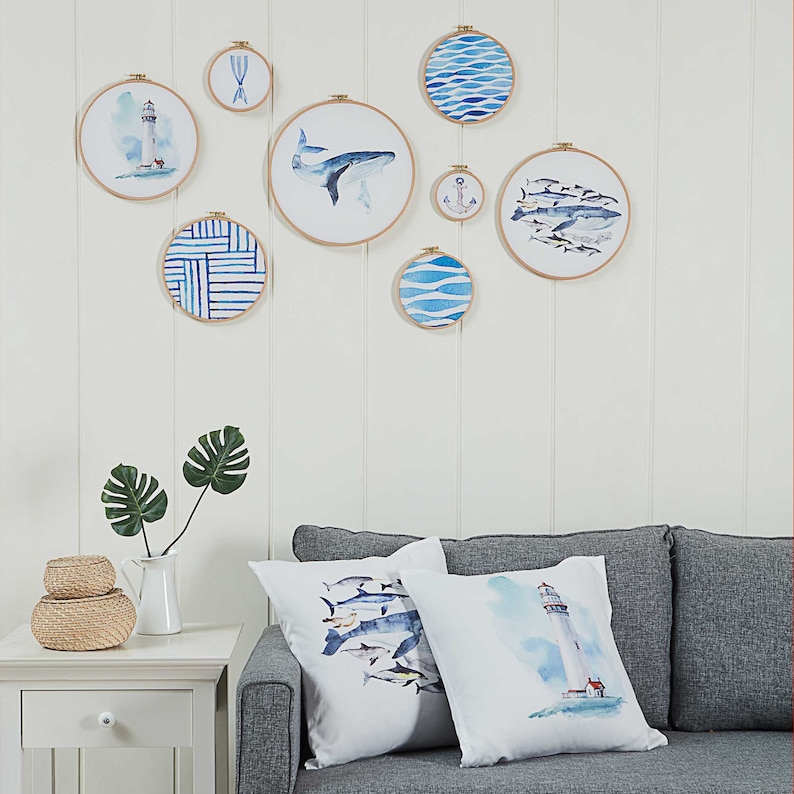 May include: A set of 9 blue and white watercolor embroidery hoops with nautical themes, including a lighthouse, an anchor, whales, and fish. The hoops are hanging on a white wall.