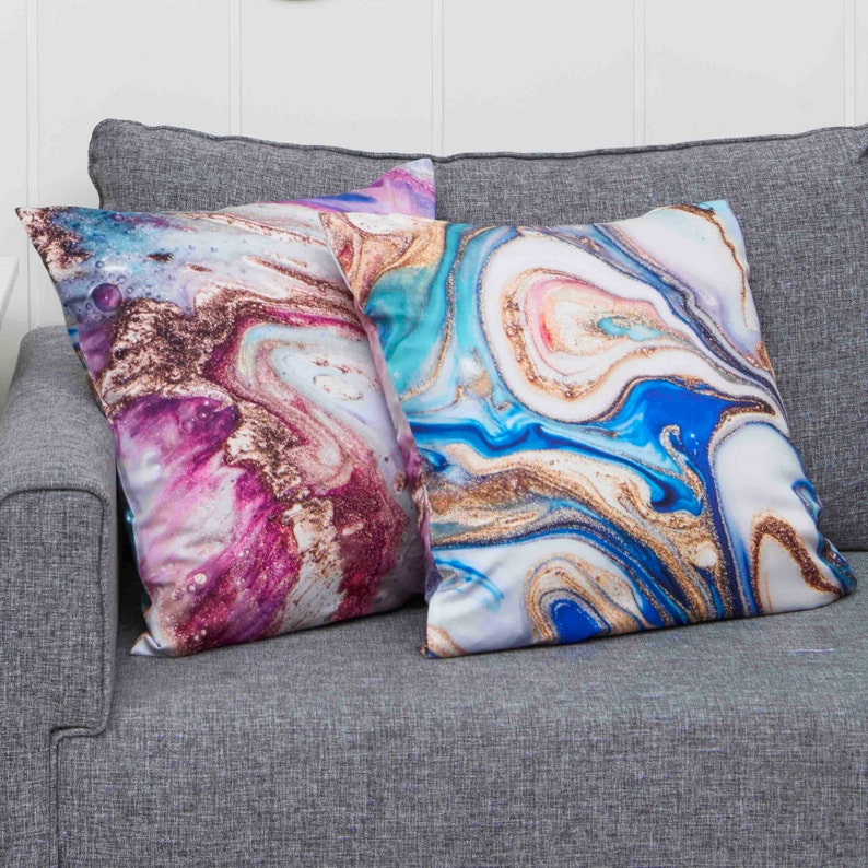 May include: Two decorative throw pillows with a marble pattern. The pillows have a white background with blue, pink, and gold swirls.