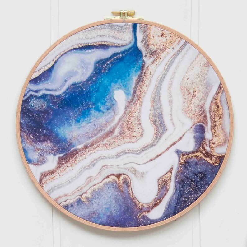 May include: A round, wooden-framed wall art piece with a blue, white, and gold abstract marbled design. The design features swirling patterns and glitter accents.