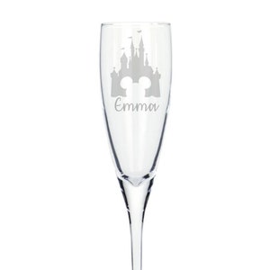 May include: A clear glass champagne flute with a silhouette of Cinderella's castle and the name "Emma" etched on the side.