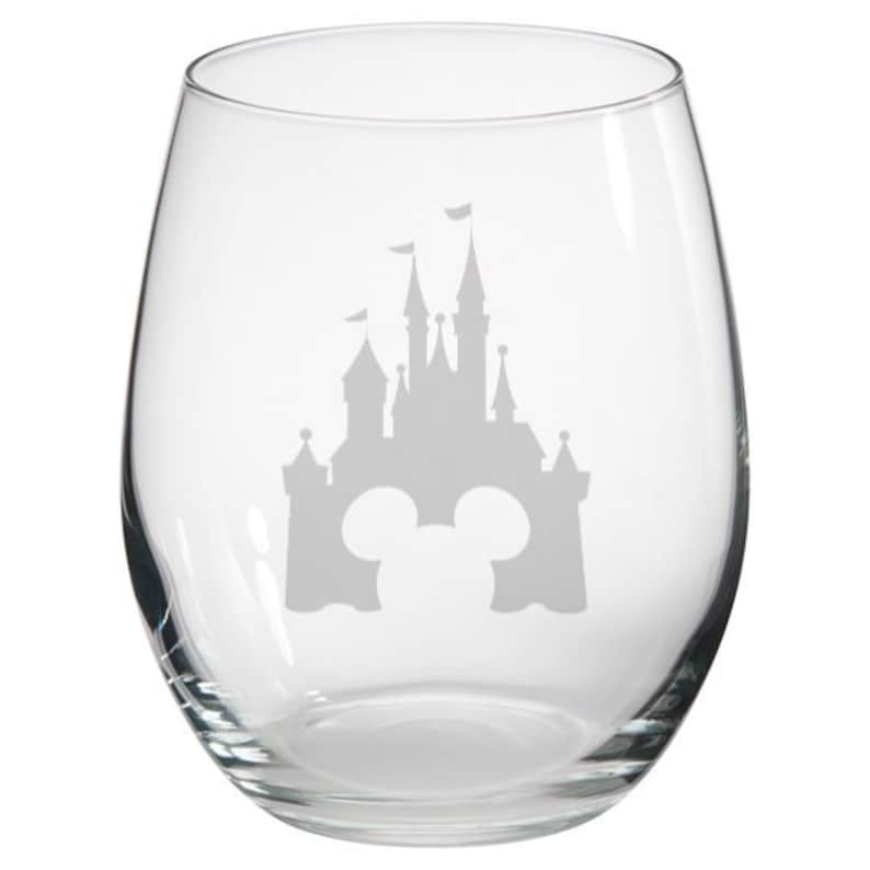 May include: A clear glass wine glass with a white silhouette of Cinderella's Castle and Mickey Mouse ears etched on the front.