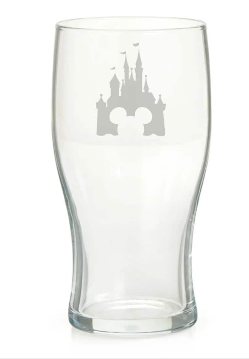 May include: A clear glass pint glass with a silhouette of Cinderella's castle and Mickey Mouse ears etched on the front.