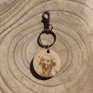 May include: A wooden keyring with a laser-engraved image of a golden retriever dog's face. The keyring has a silver metal ring and a silver metal clasp.