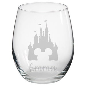 May include: Clear glass wine glass with a gray silhouette of Cinderella's castle and Mickey Mouse ears, and the name "Emma" etched on the bottom.
