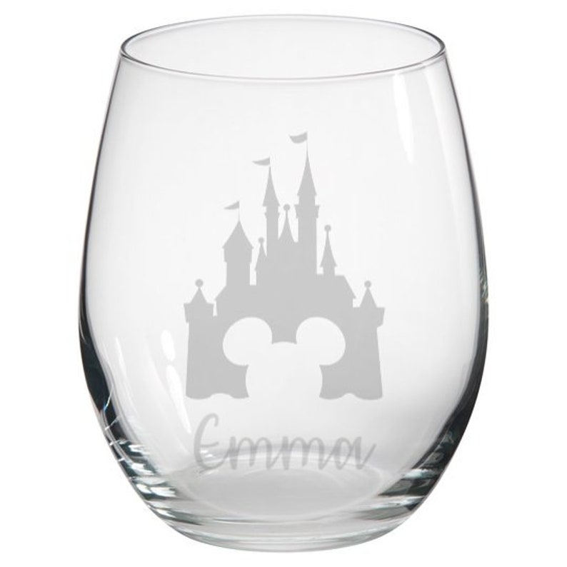 May include: Clear glass wine glass with a gray silhouette of Cinderella's castle and Mickey Mouse ears, and the name "Emma" etched on the bottom.