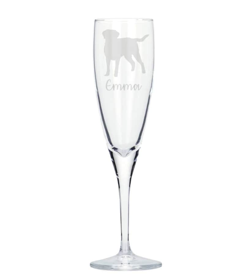 May include: A clear glass champagne flute with an etched silhouette of a Labrador Retriever and the name "Emma" underneath.