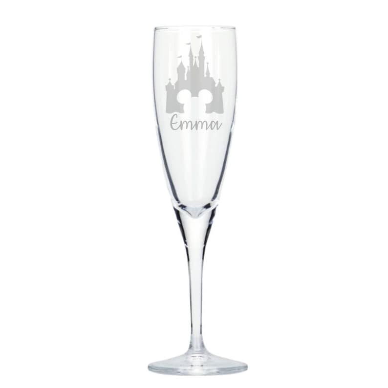 May include: A clear glass champagne flute with a silhouette of Cinderella's castle and the name "Emma" etched on the side.