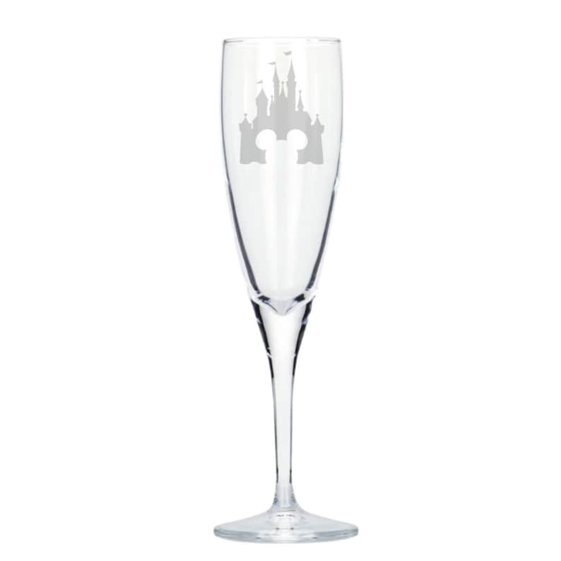 May include: A clear glass champagne flute with an etched design of the Cinderella Castle from Disney World. The castle is outlined in silver and has the iconic Mickey Mouse ears at the top.