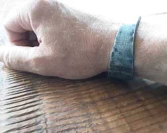 May include: A close-up of a person's wrist wearing a dark blue leather bracelet with a cracked texture.