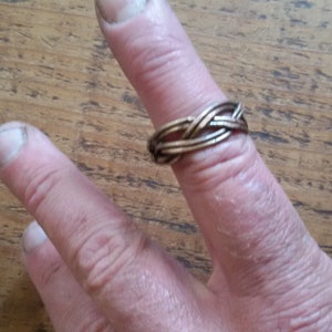 Peut inclure: Une bague en métal tressé avec un motif tissé. La bague est portée à un doigt.