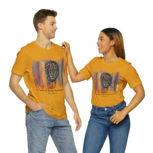 May include: Two people wearing mustard yellow t-shirts with a colourful abstract background and a lion graphic. The text on the shirt reads "The Lion of Judah Has Conquered, Revelation 5:5".