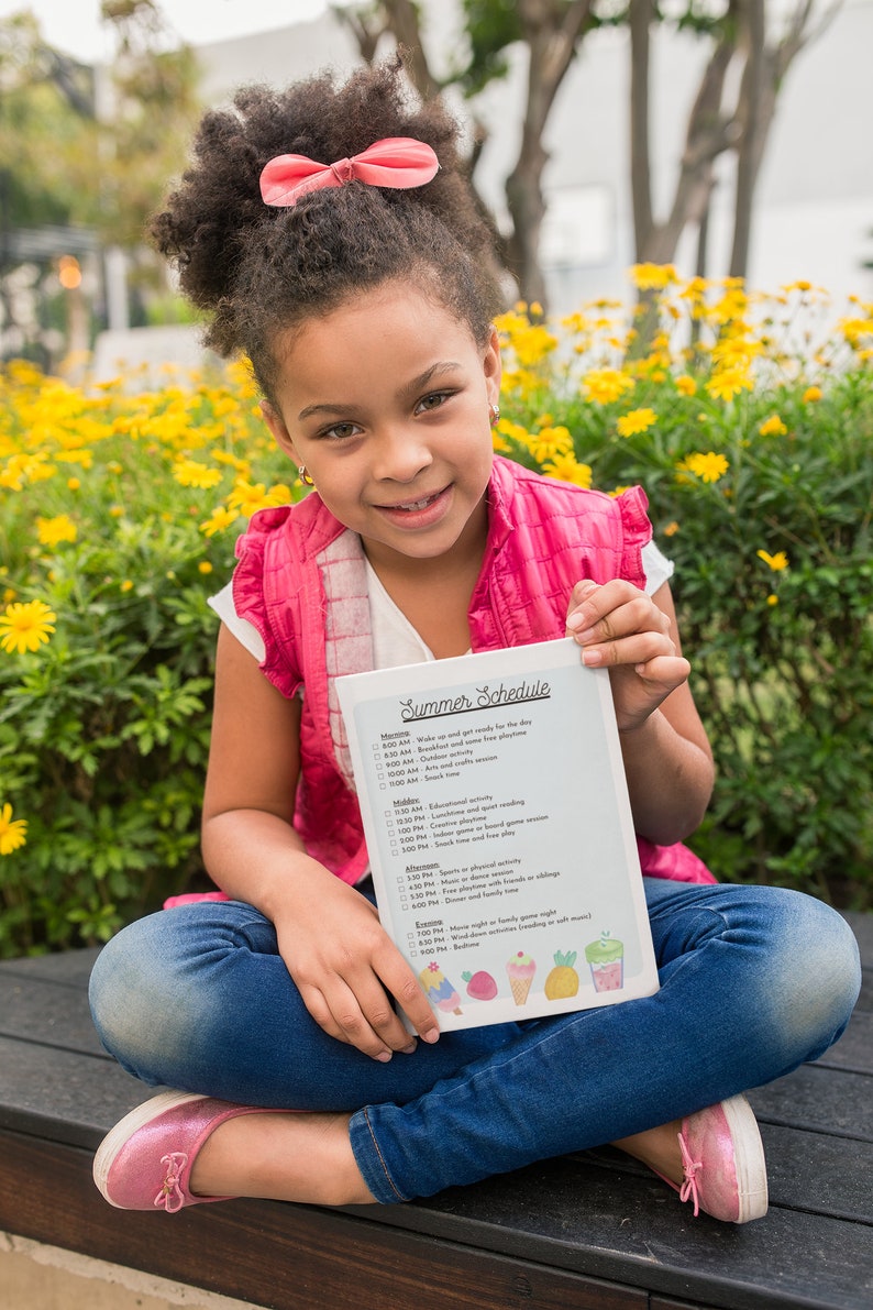 May include: A young girl wearing a pink shirt and blue jeans sits on a wooden bench holding a white sheet of paper with a summer schedule written on it. The schedule includes activities like wake up, breakfast, outdoor playtime, arts and crafts, lunch, educational activity, indoor playtime, snack time, sports or physical activity, free time, dinner, family time or siblings, movie night or family game night, bedtime.