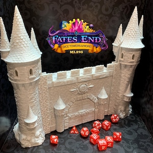 May include: A light-colored castle dice tower with two tall towers and a central wall with a gate. The text "FATES END DICE TOWERS & MORE!" is visible. Several red dice are scattered in front of the tower.
