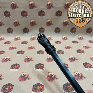 May include: A black plastic hand with four fingers, attached to a black plastic rod. The hand is pointing upwards.