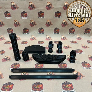 May include: A 3D printed miniature display stand for a miniature figure. The stand features a black base with a winged eagle design, two black rods, and two black hands. The stand is designed to hold a miniature figure in a standing position.