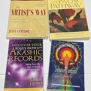 May include: Four books with colorful covers are displayed. Titles include "The Artist's Way," "The Psychic Pathway," "Discover Your Akashic Records," and "The Projection of the Astral Body." The books are on a white surface.