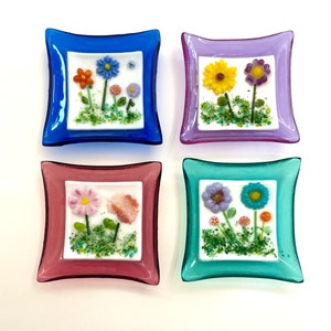 May include: Four small glass dishes with a white background and colorful flower designs. The dishes are blue, purple, pink, and green.