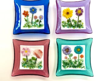 May include: Four small glass dishes with a white background and colourful flower designs. The dishes are blue, purple, pink, and green.