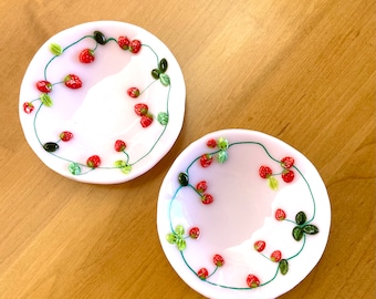 May include: Two white ceramic plates with a green vine and red strawberry design.