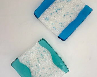 May include: Two square glass dishes with white speckled glaze and blue accents. The larger dish has a blue stripe across the top and bottom. The smaller dish has a wavy blue line across the centre.
