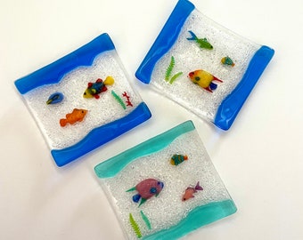 May include: Three small glass dishes with blue and turquoise borders. Each dish features a white background with a sparkly texture and colourful glass fish and seaweed.
