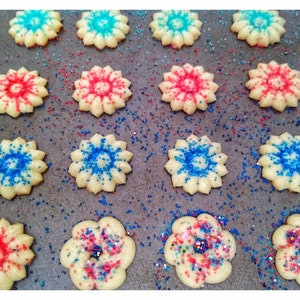 May include: A baking sheet with a variety of star-shaped cookies decorated with red, blue, and white sprinkles. The cookies are arranged in rows on a baking sheet lined with parchment paper.