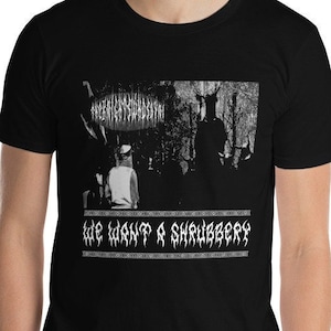 May include: Black t-shirt with a grayscale graphic of figures in a forest and the text "WE WANT A SHRUBBERY" in a white, stylized font. The shirt is short-sleeved and appears to be made of a soft material.