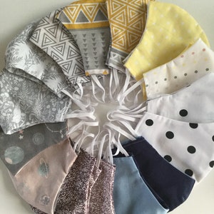 May include: A collection of 10 fabric face masks with various patterns, including geometric, floral, and polka dot designs. The masks are arranged in a circle, with the colors ranging from light gray to yellow.
