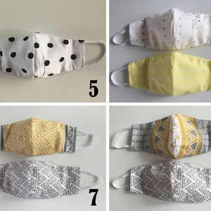 May include: Four different styles of face masks. The first mask is white with black polka dots, the second is yellow with white polka dots, the third is gray with a yellow geometric pattern, and the fourth is white with a gray geometric pattern.