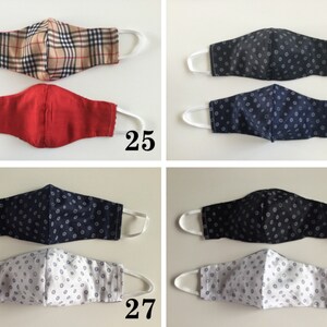 May include: Four different fabric face masks with various patterns. The first mask is a plaid pattern in brown and beige. The second mask is a solid red color. The third mask is a dark blue with a white polka dot pattern. The fourth mask is a white with a dark blue polka dot pattern.