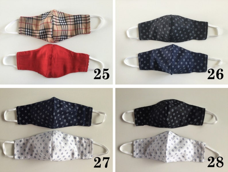 May include: Four different fabric face masks with various patterns. The first mask is a plaid pattern in brown and beige. The second mask is a solid red color. The third mask is a dark blue with a white polka dot pattern. The fourth mask is a white with a dark blue polka dot pattern.
