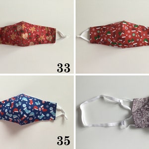May include: Four different Christmas-themed face masks. The first mask has a red background with gingerbread men and candy canes. The second mask has a red background with snowflakes and Christmas hats. The third mask has a blue background with snowflakes and Christmas stockings. The fourth mask is a solid gray color.