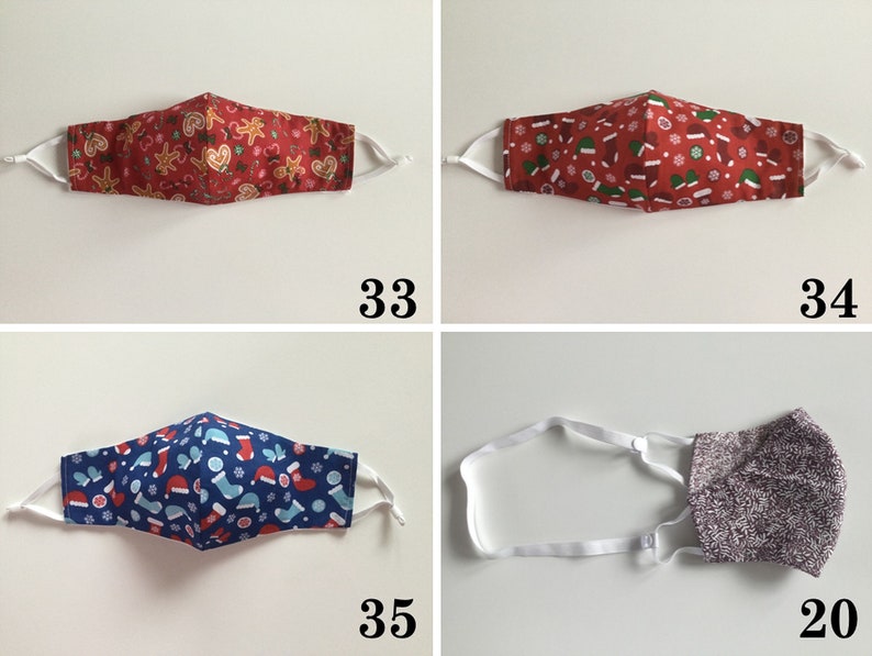 May include: Four different Christmas-themed face masks. The first mask has a red background with gingerbread men and candy canes. The second mask has a red background with snowflakes and Christmas hats. The third mask has a blue background with snowflakes and Christmas stockings. The fourth mask is a solid gray color.