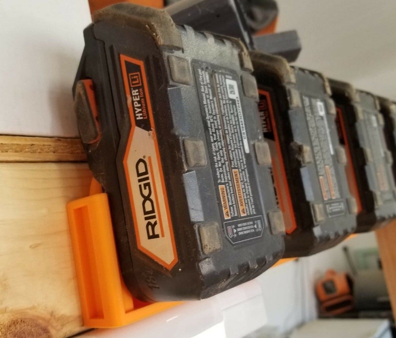 May include: A set of four orange and black Ridgid HYPER Lithium-Ion batteries mounted on a wall-mounted orange plastic holder.