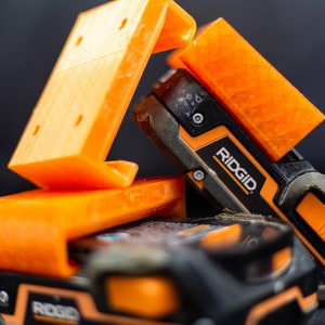 May include: Two orange 3D printed battery holders with a black and orange Ridgid power tool battery.