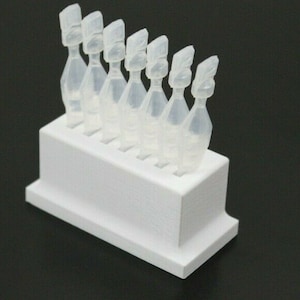 Puede incluir: Un dispensador de plástico blanco con siete botellas de plástico transparente para gotas para los ojos.
