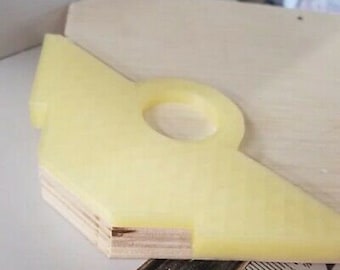 May include: A yellow plastic woodworking jig with a hole in the center. The jig is attached to a piece of plywood.