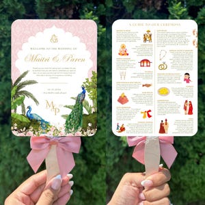 May include: A wedding fan with a pink bow. The fan features text that reads "Welcome to the Wedding of Maitri & Paren" and "10.19.2024". The design includes illustrations of peacocks and floral elements.
